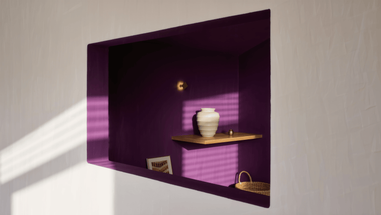 A shallow wall recess painted deep plum, holding a sculptural vessel on a floating oak shelf lit by a small picture light.