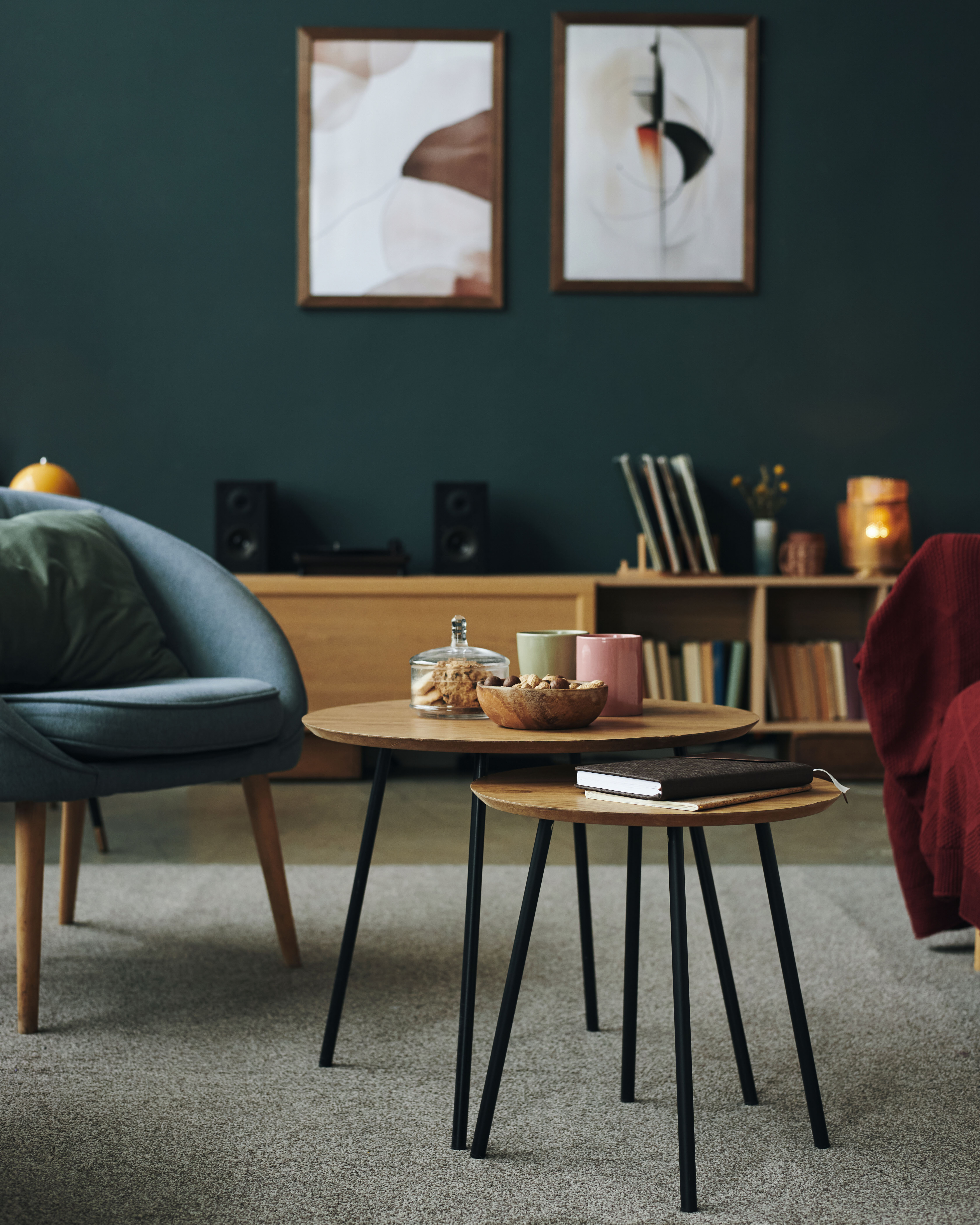 A dark emerald wall anchors a compact bookshelf and vinyl-record nook beside a burgundy accent chair and a wood-and-iron coffee table.