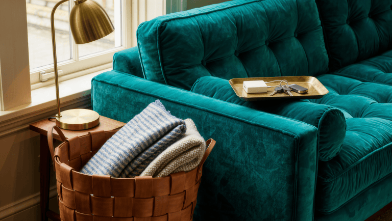 A small brass side table beside an armchair holds a crystal glass, reading glasses on an open book, and a bronze dish.
