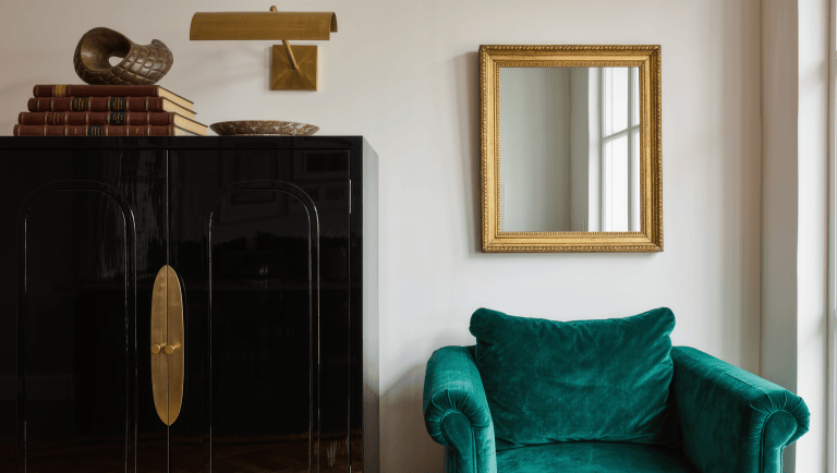 A tall lacquered black cabinet with brass hardware anchors one side of a room while a pale wall with a gilt mirror balances it.