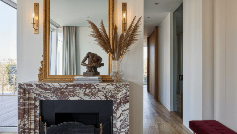 A marble fireplace mantel dressed with a mirror and bronze objects sits beside a clear doorway walking path.