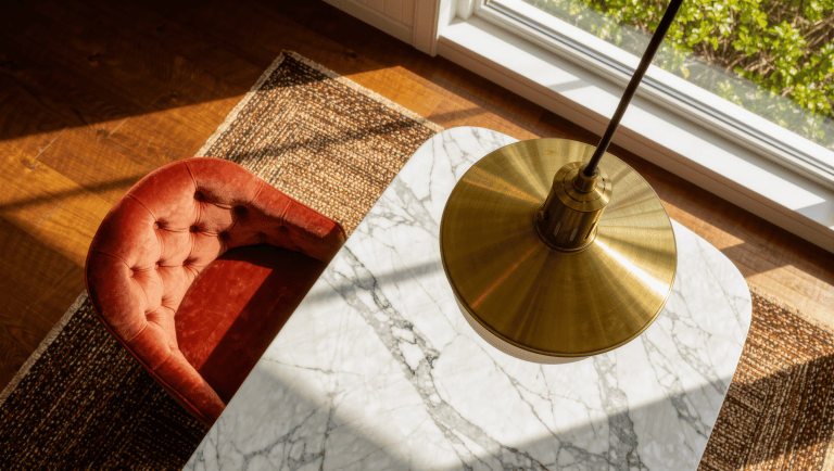 A tufted velvet dining chair pulled fully back from a marble table to show its clearance, beneath a brass pendant light and a runner rug.