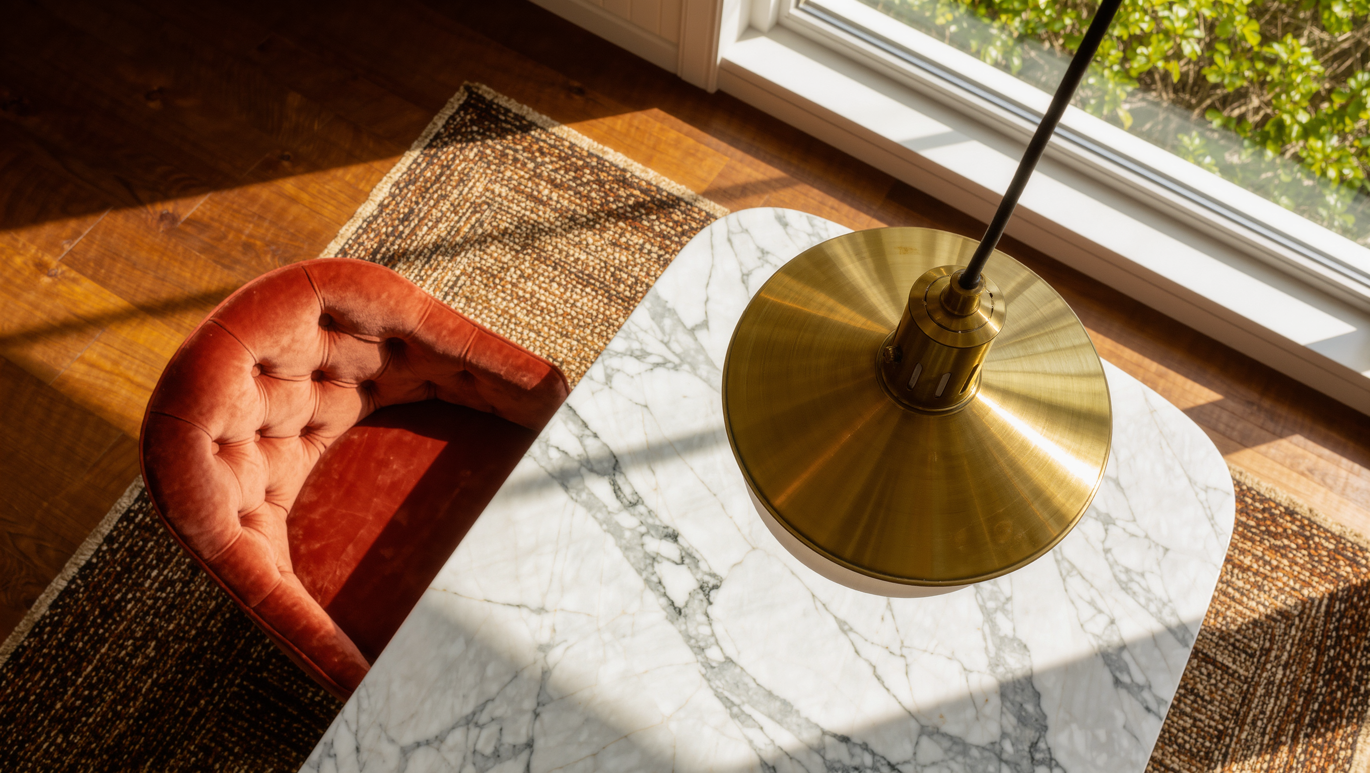 A tufted velvet dining chair pulled fully back from a marble table to show its clearance, beneath a brass pendant light and a runner rug.