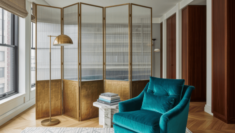 A tall freestanding brass and glass screen creates a room boundary in an open-plan space without attaching to any wall.