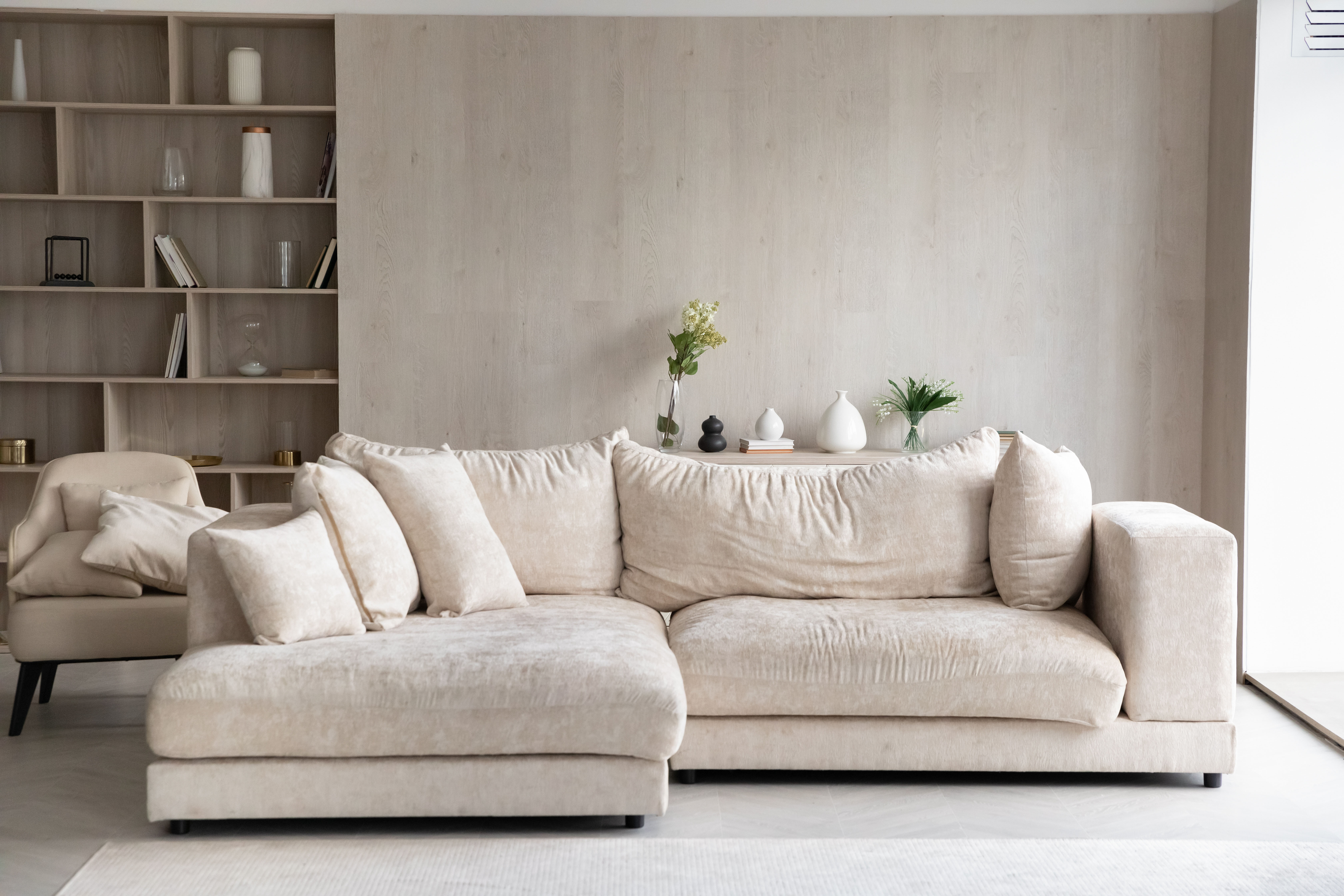 A cream sectional sofa sits beside a built-in bookcase filled with books and decorative objects, with a styled console table and sheer-curtained window completing the layered living room.