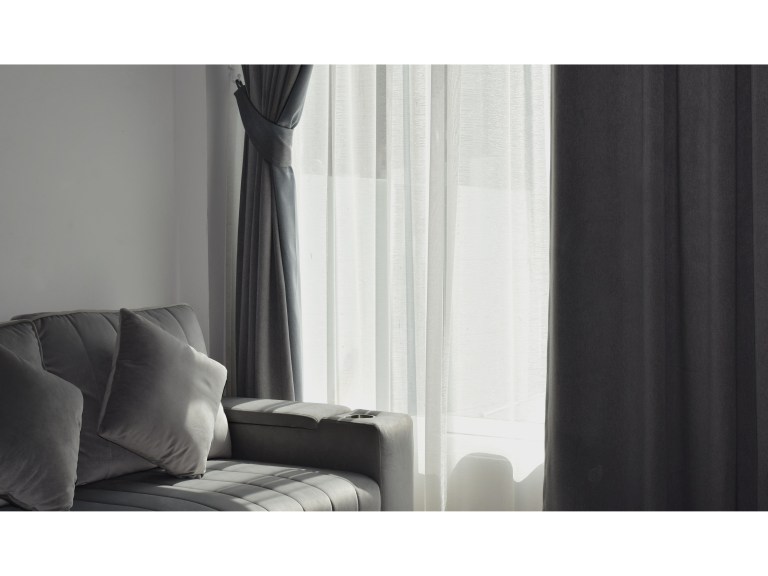 Floor-to-ceiling charcoal-gray curtains framing a tall window with sheer inner panels, tied back beside a tailored gray sofa.