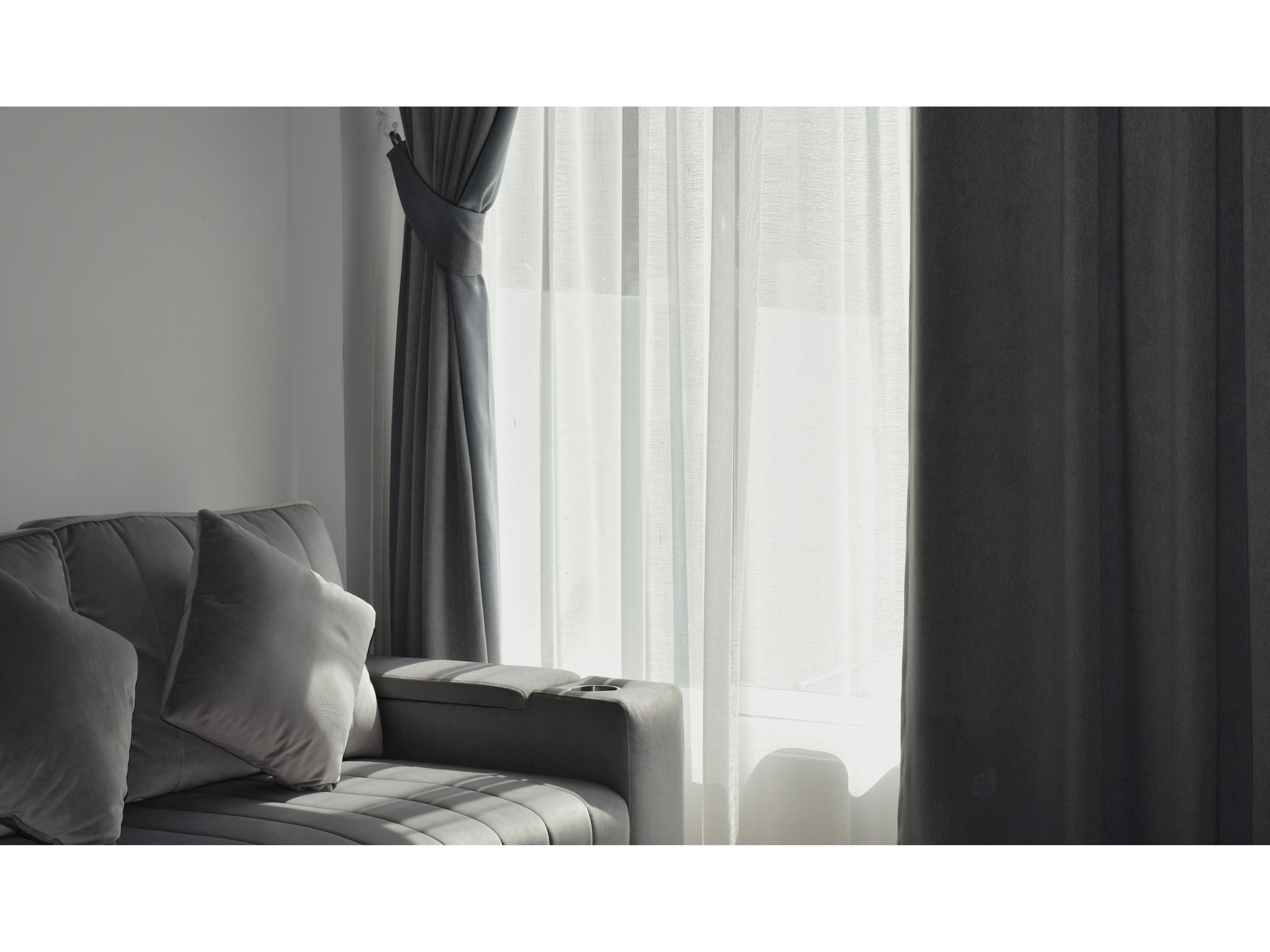 Floor-to-ceiling charcoal-gray curtains framing a tall window with sheer inner panels, tied back beside a tailored gray sofa.