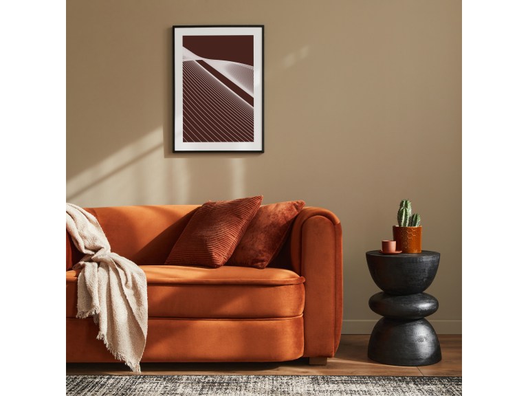 A burnt-orange velvet sofa with a draped throw and rust cushions, a round side table holding a potted plant nearby.