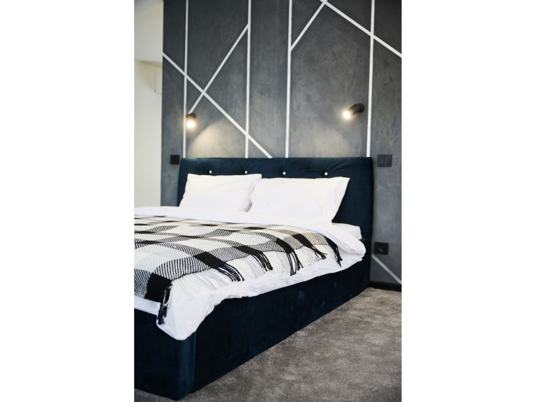 A tufted navy velvet bed set against a bold charcoal geometric accent wall, dressed in crisp white linens and a graphic throw.