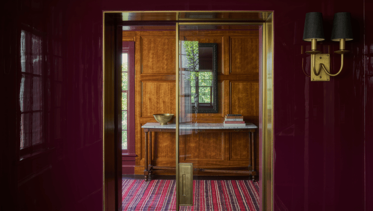 A slim brass-framed pocket door slid fully open into a lacquered plum wall pocket, revealing a marble-top console behind it.
