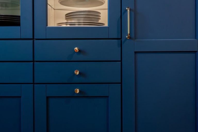 A close-up of navy blue built-in cabinetry with brass pulls and a glass-front cabinet displaying white dishware.