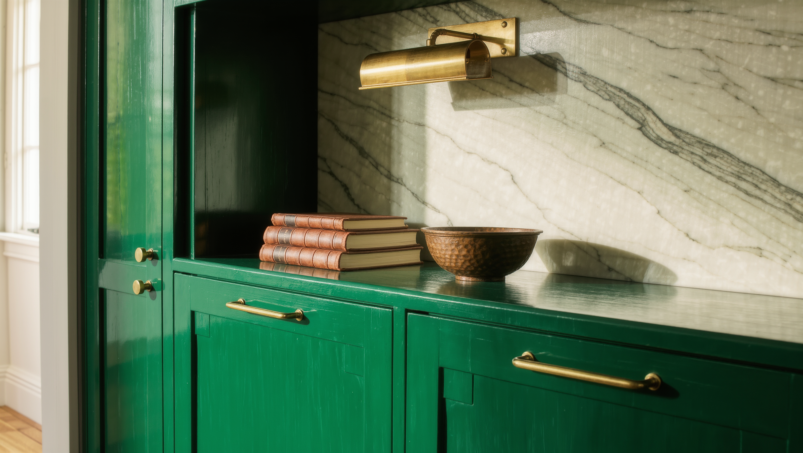 Closed emerald lacquered cabinets stay shut below while an open shelf above displays books and a bronze bowl.