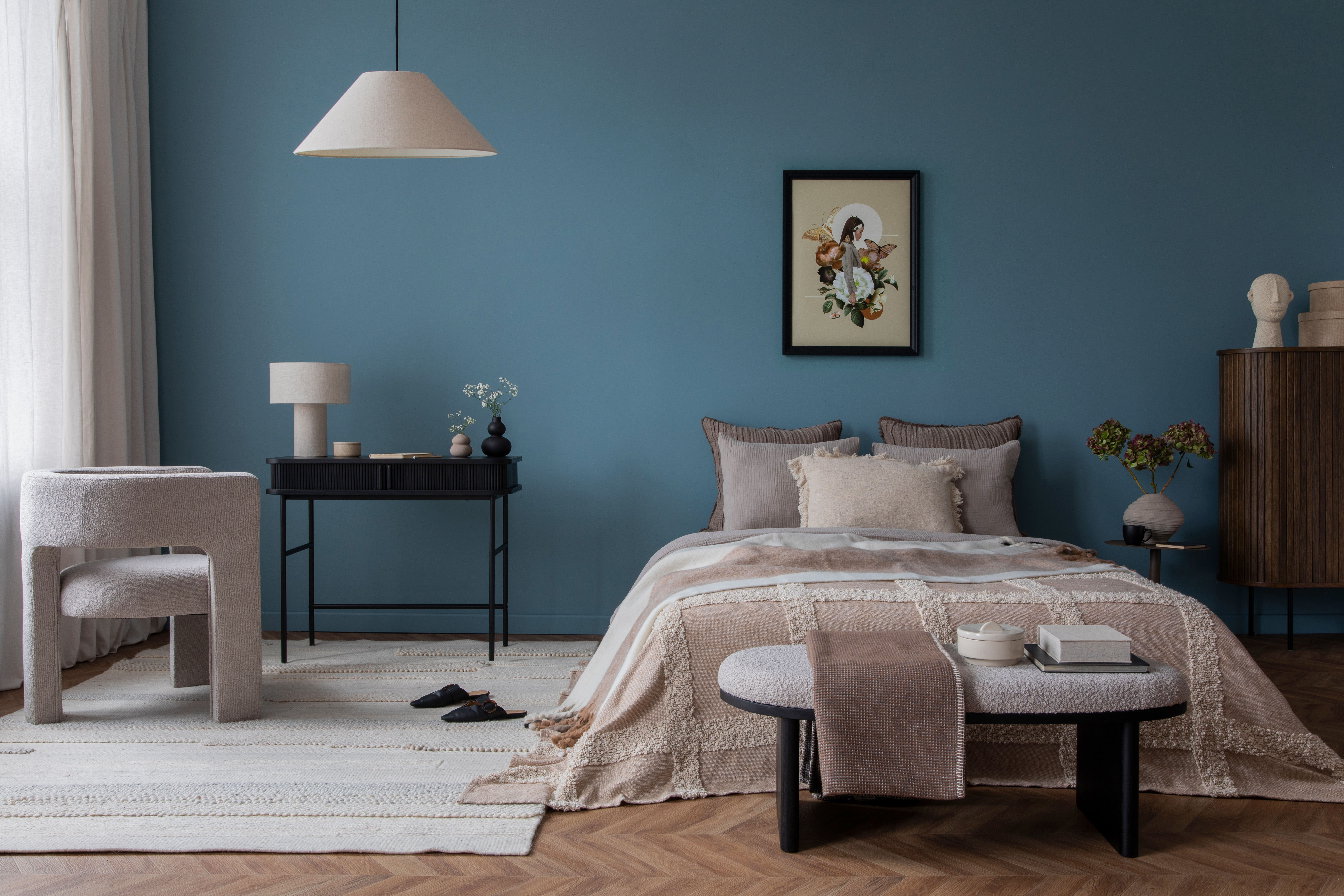 A black desk with a table lamp sits against a deep teal bedroom wall beside a layered, textile-rich bed.
