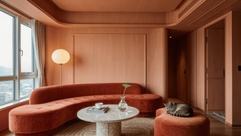 A compact living room with a terracotta curved sofa, round travertine table, and kidney-shaped ottoman easing the walking path.