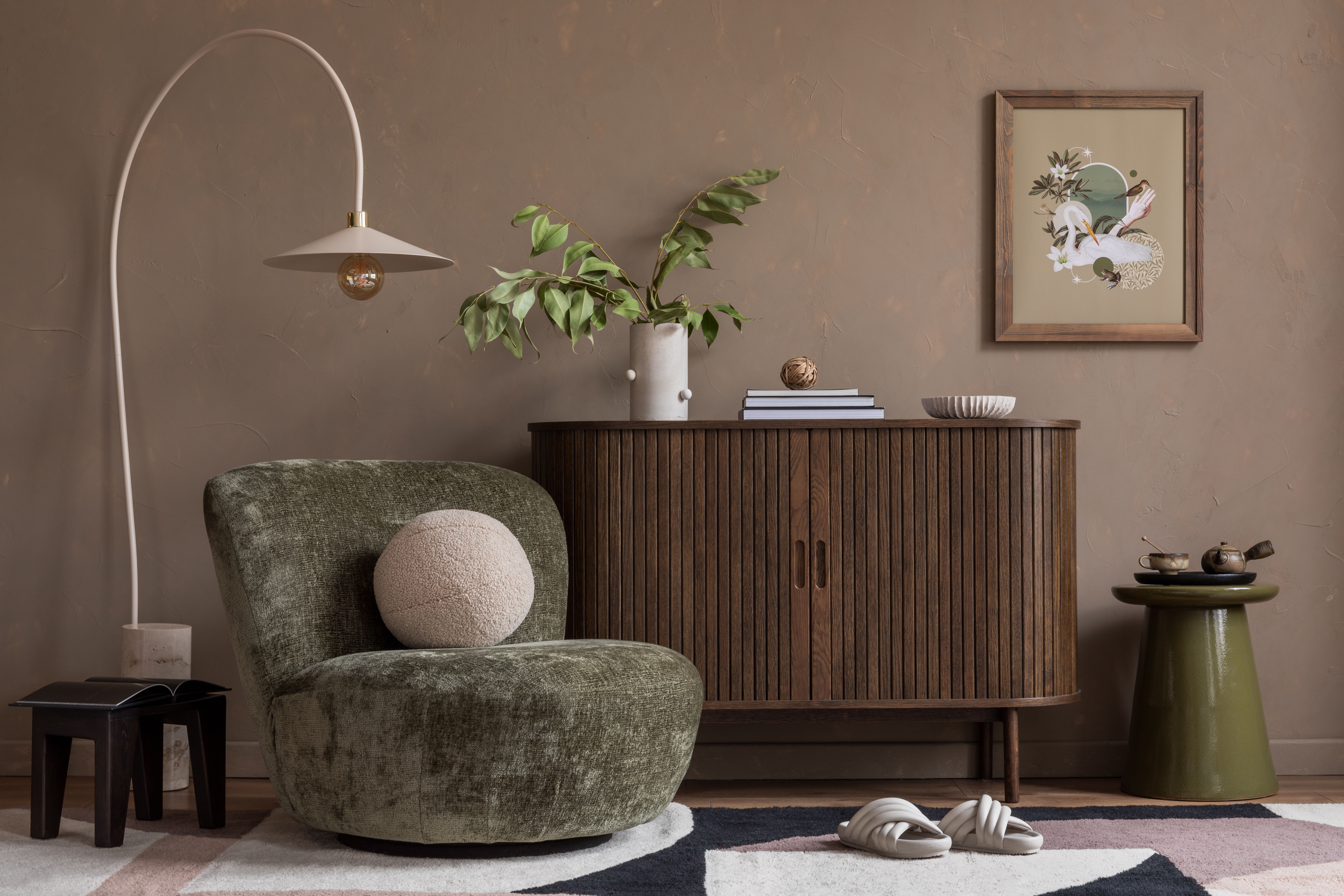 An olive-green curved swivel chair and a fluted wood sideboard with framed art sit against a warm terracotta wall.