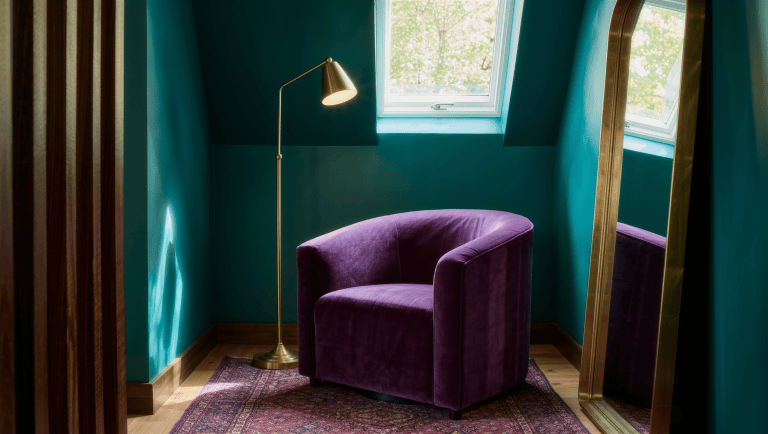 An oversized aubergine velvet armchair on a jewel-toned rug in a compact sitting room corner.