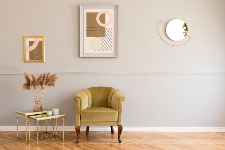 An olive velvet armchair sits beside a round mirror and a gallery of framed prints, with a brass-legged side table completing the corner.