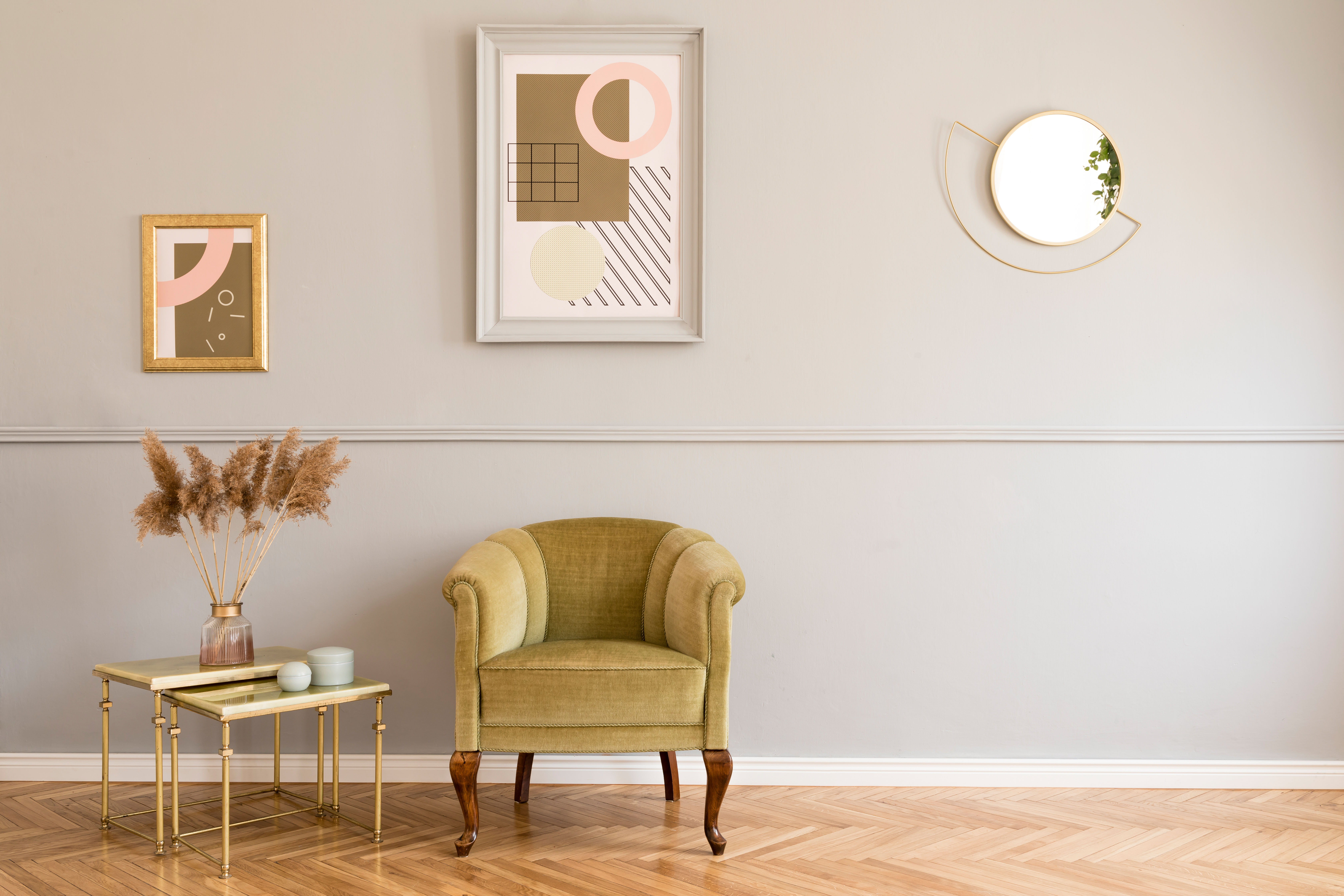 An olive velvet armchair sits beside a round mirror and a gallery of framed prints, with a brass-legged side table completing the corner.