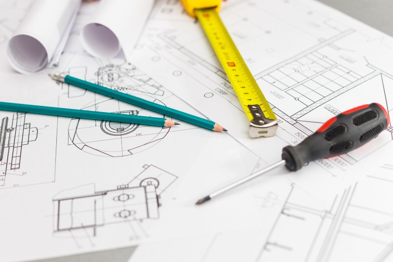 Rolled blueprints, a yellow tape measure, sketching pencils, and a screwdriver laid out over architectural floor plan drawings.