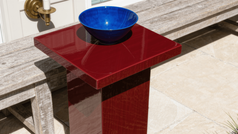 An oxblood lacquer outdoor side table beside a weathered teak bench on limestone
