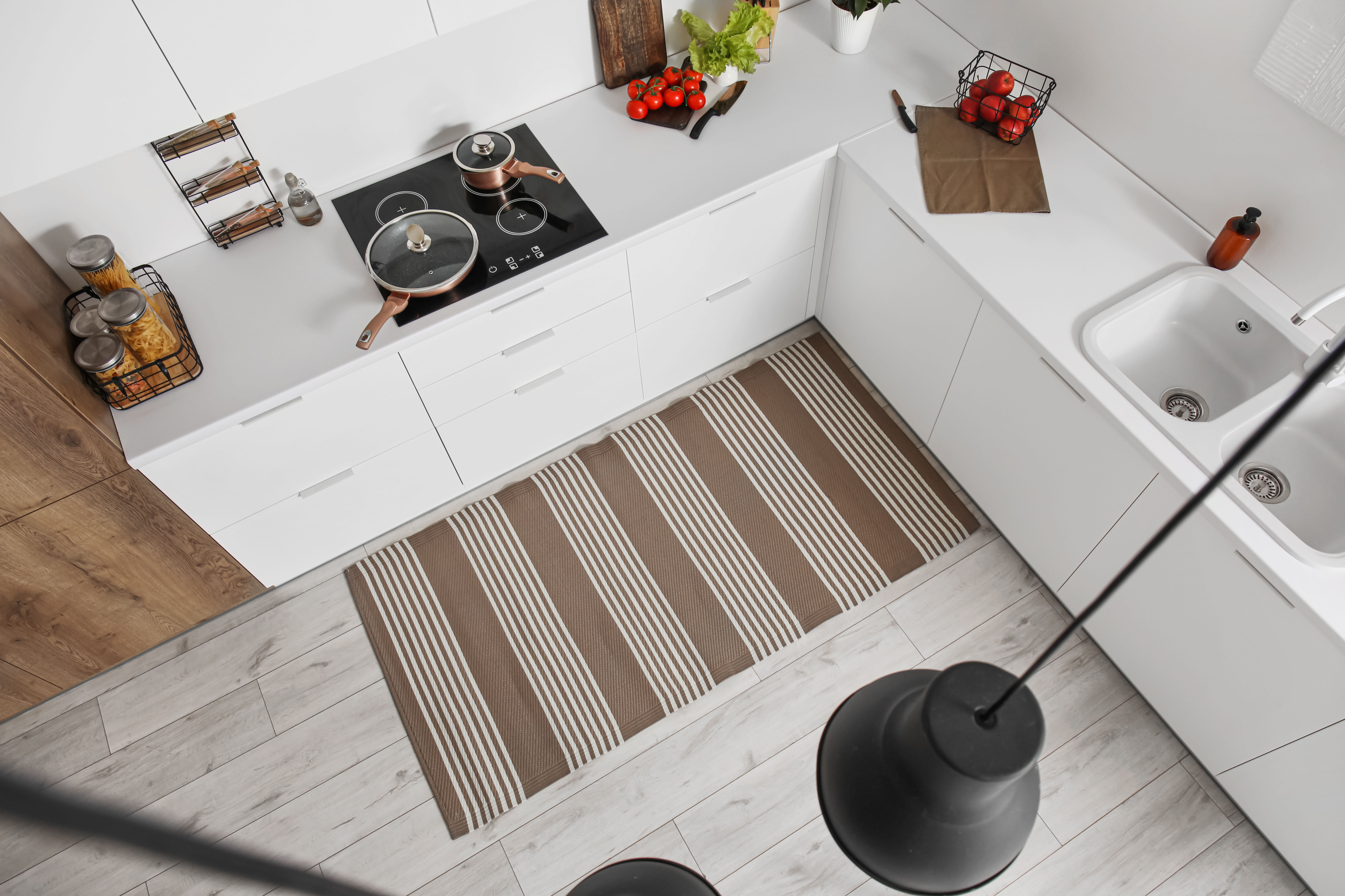 A striped woven runner laid across a crisp white galley kitchen floor, seen from above between the cabinetry and sink.