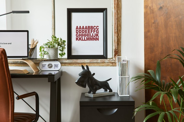 A wood-paneled office nook with a slim writing desk, a leather chair, and a gallery wall of framed art beside a small bronze dog sculpture.