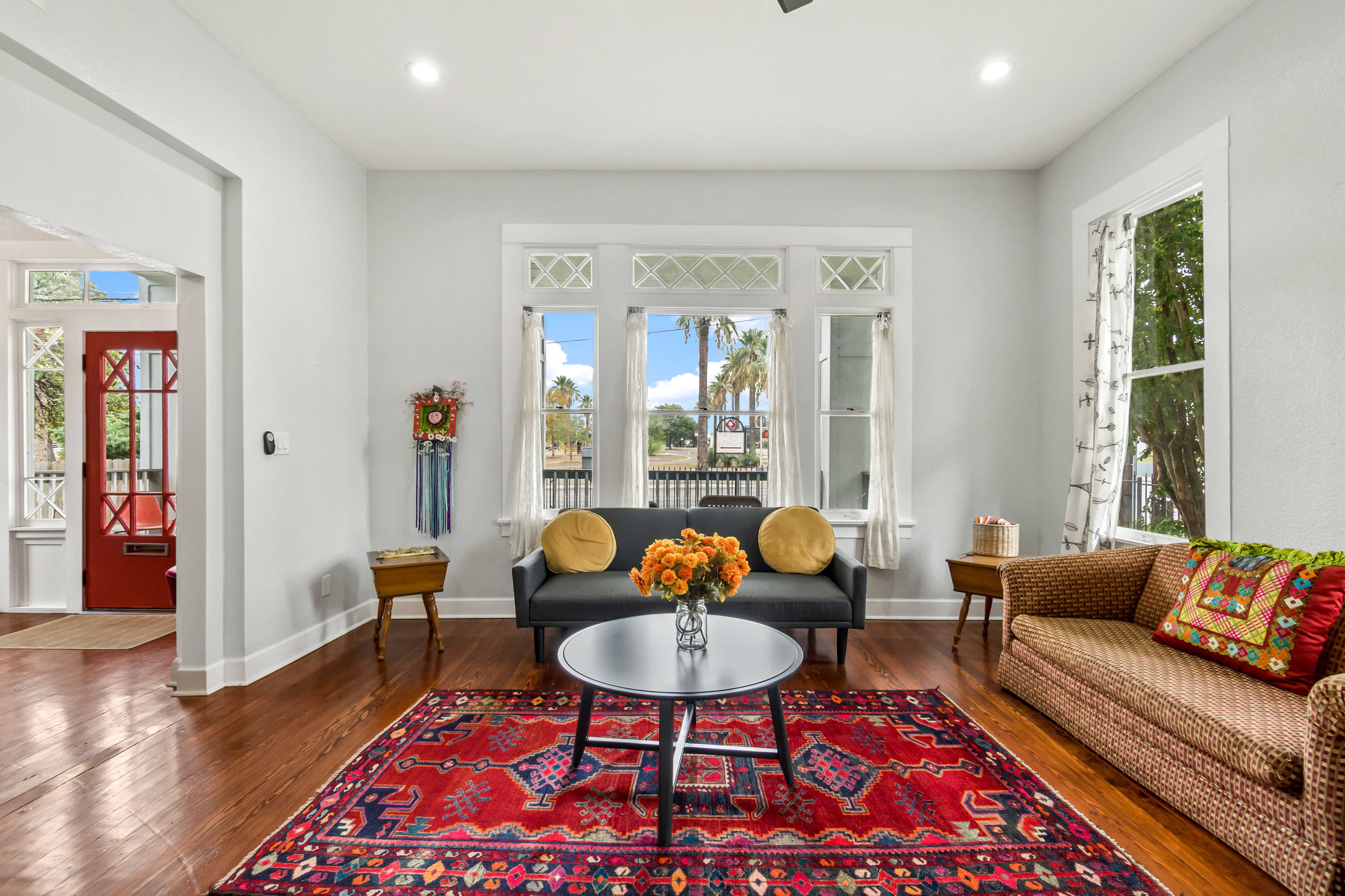 A richly patterned red and navy rug anchors a pair of upholstered chairs in front of ornate stained-glass windows, with gilt-framed art and warm wood floors completing the room.