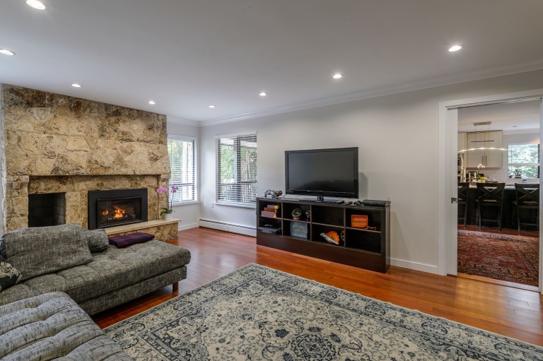 A stone fireplace sits off to one side of the wall while a patterned area rug and grey sectional gather the seating group in front of it.
