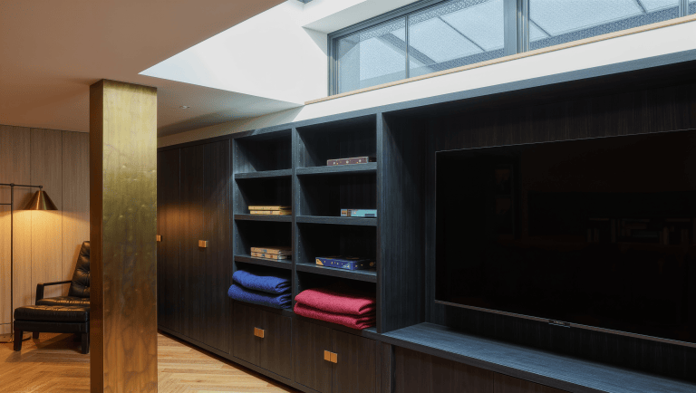 A charcoal storage unit and brass-clad column separate a basement television zone from a reading area.