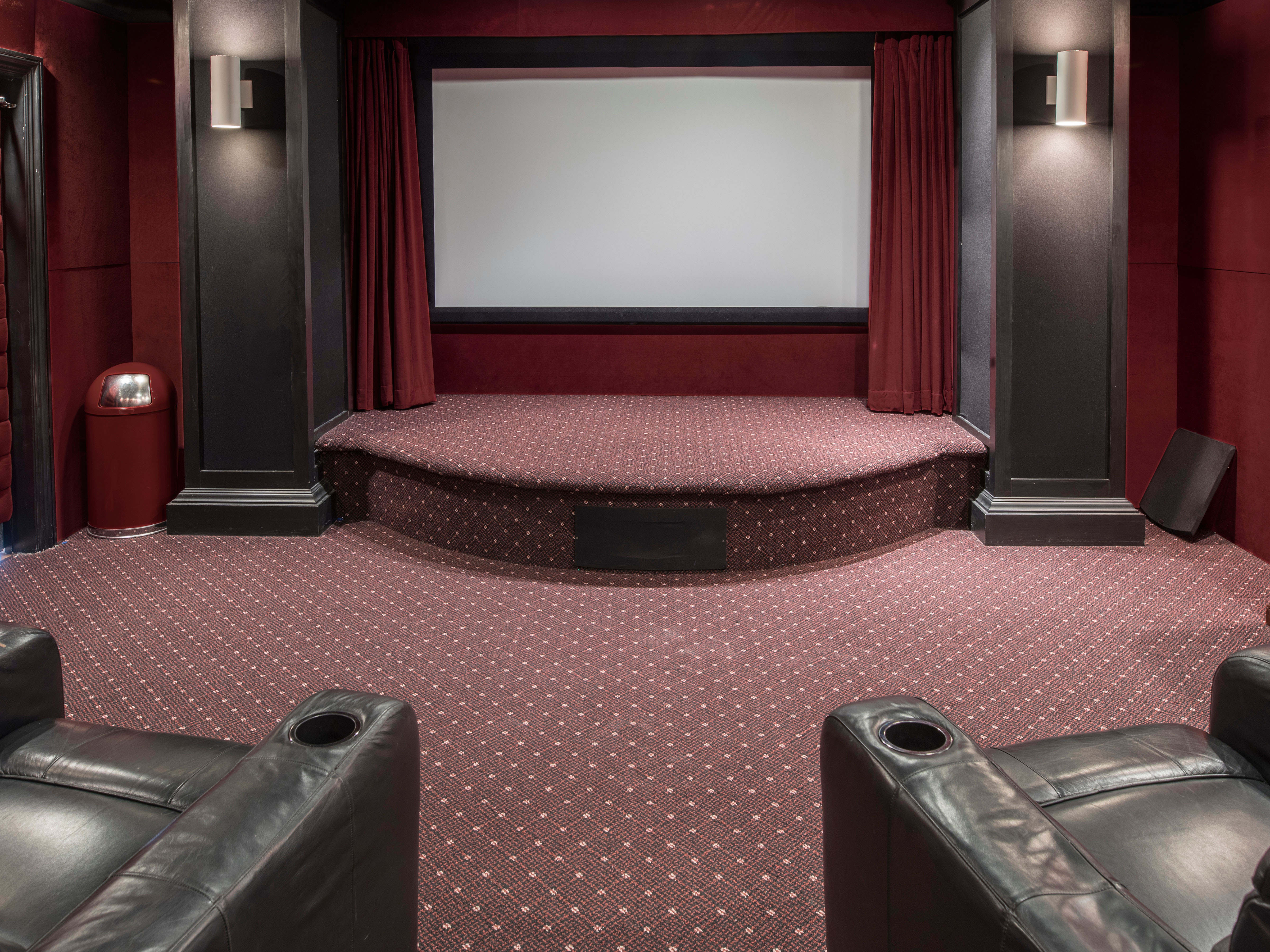 Tiered leather theater seating faces a screen framed by burgundy curtains and paneled columns in a home theater.