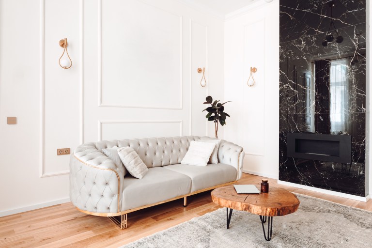 A tufted velvet sofa anchors a wall paneled in white millwork, facing a black veined marble accent wall with brass sconces and a round wood coffee table.