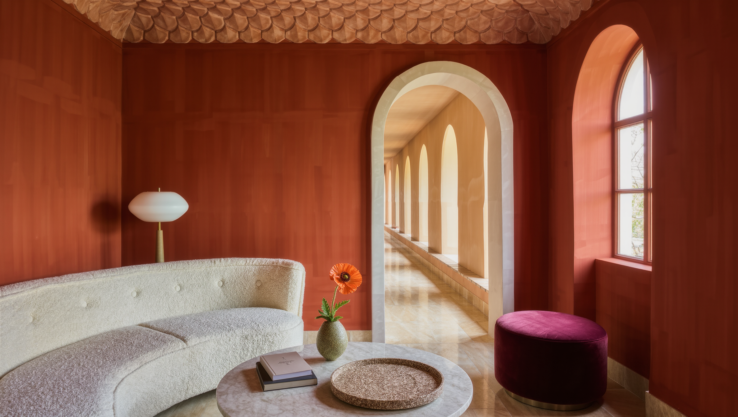 A room with an arched doorway, curved ivory boucle sofa, round travertine table, scalloped ceiling detail, and warm arched-window daylight.