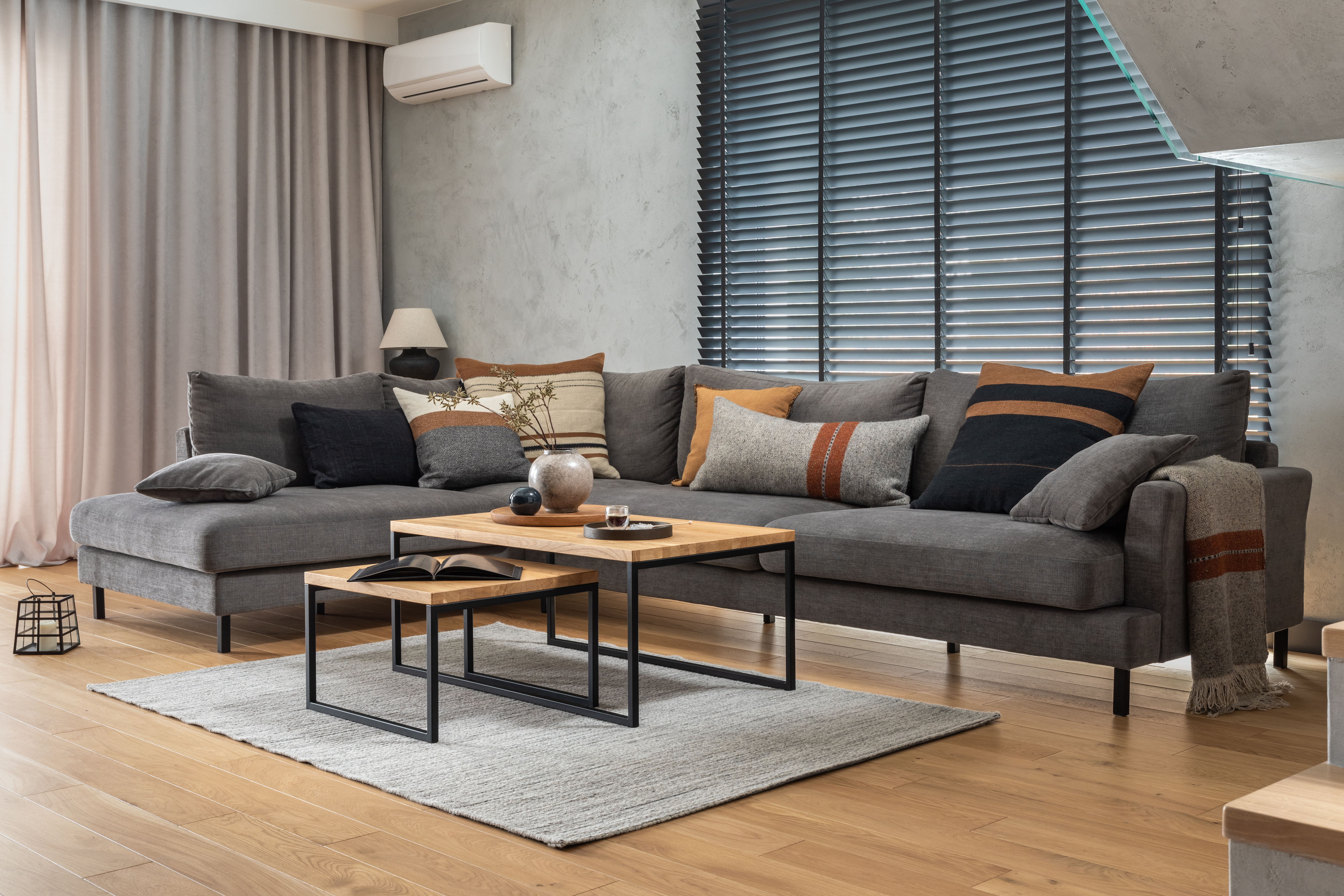 A layered area rug, a rust-and-charcoal patterned pillow arrangement, and a knit throw soften a gray sectional sofa against an otherwise hard-floored room.