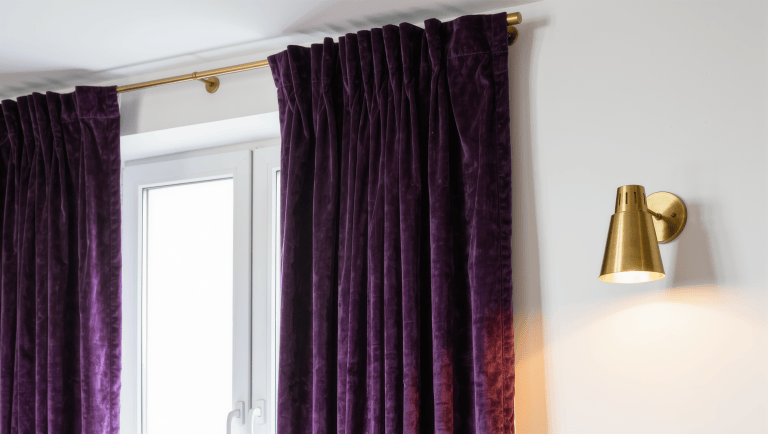 Floor-to-ceiling aubergine curtains hung high on a brass tension rod above a rental window