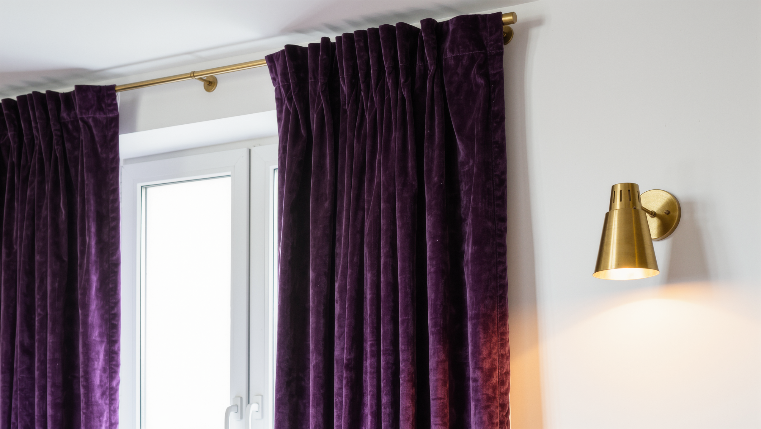 Floor-to-ceiling aubergine curtains hung high on a brass tension rod above a rental window