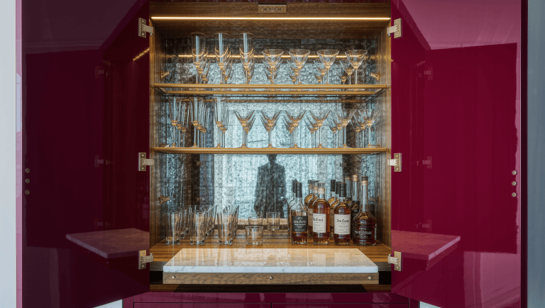 A lacquered burgundy closet bar opens to reveal mirrored shelves of glassware and bottles.