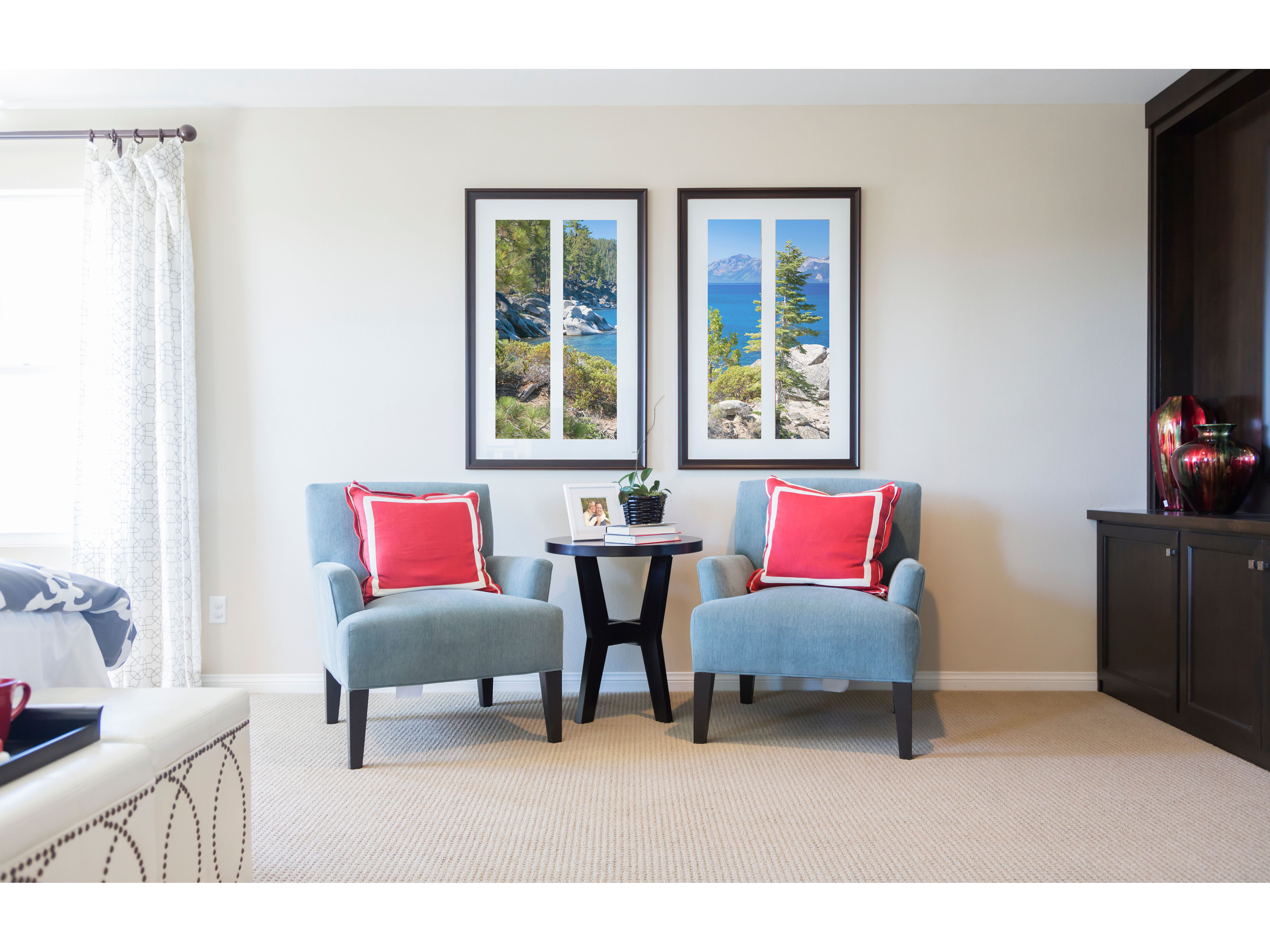 Two blue accent chairs and a round side table form a small sitting nook beneath a pair of framed seascapes.