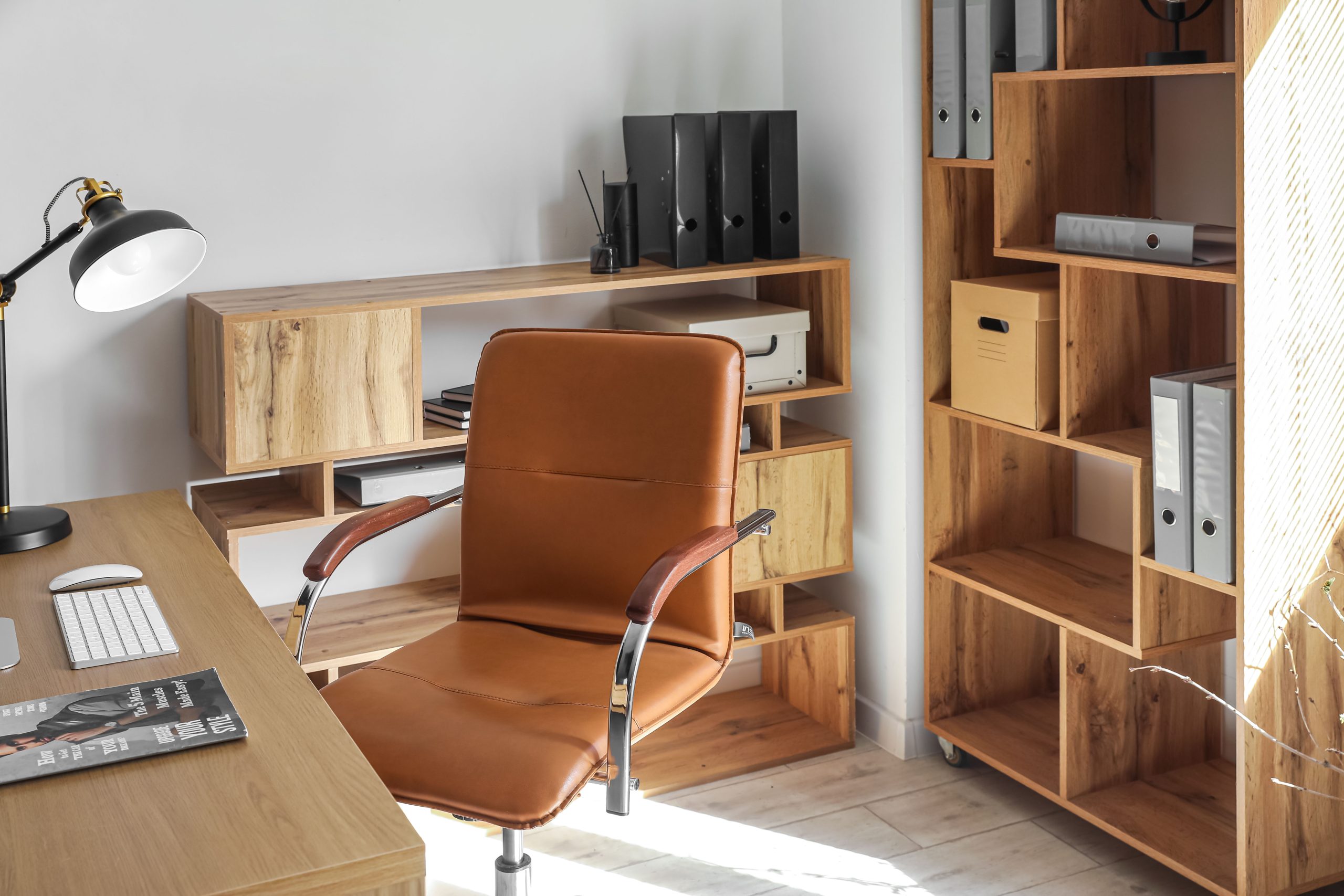 A cognac leather office chair sits at a wood desk with a clear path to the built-in shelving and box files behind it.