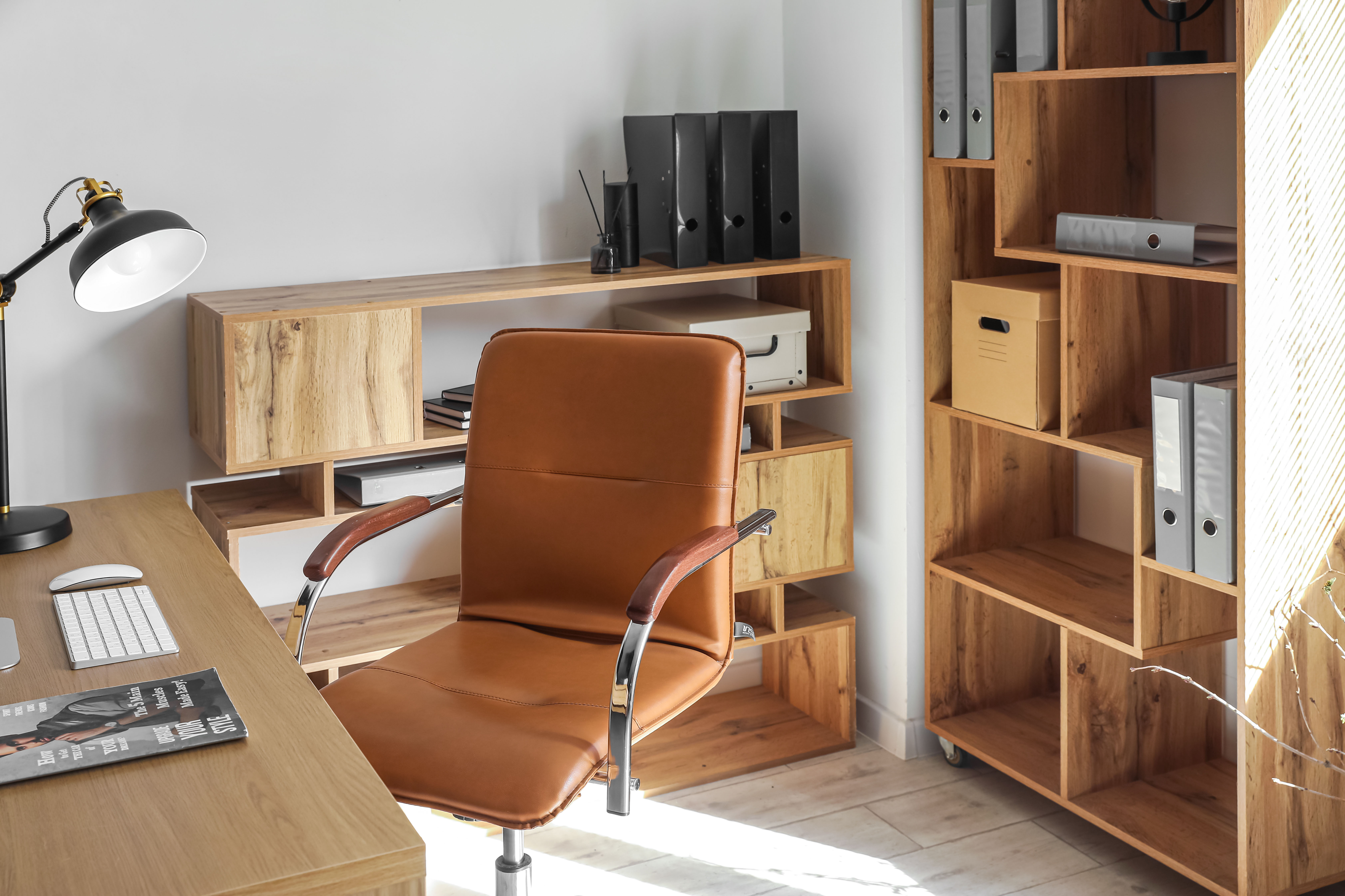 A cognac leather office chair sits at a wood desk with a clear path to the built-in shelving and box files behind it.