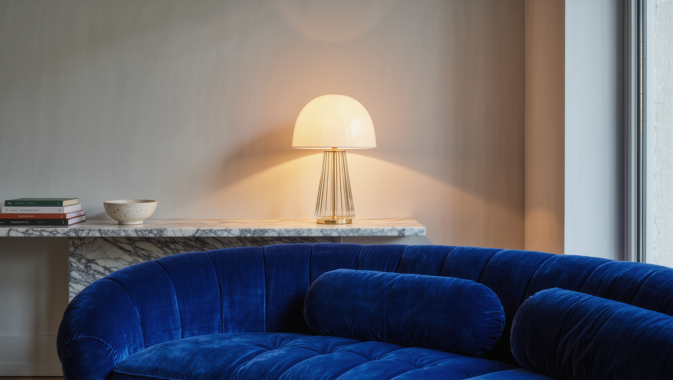 A cordless fluted-glass lamp glows on a floating marble console behind a velvet sofa, with no visible cord.