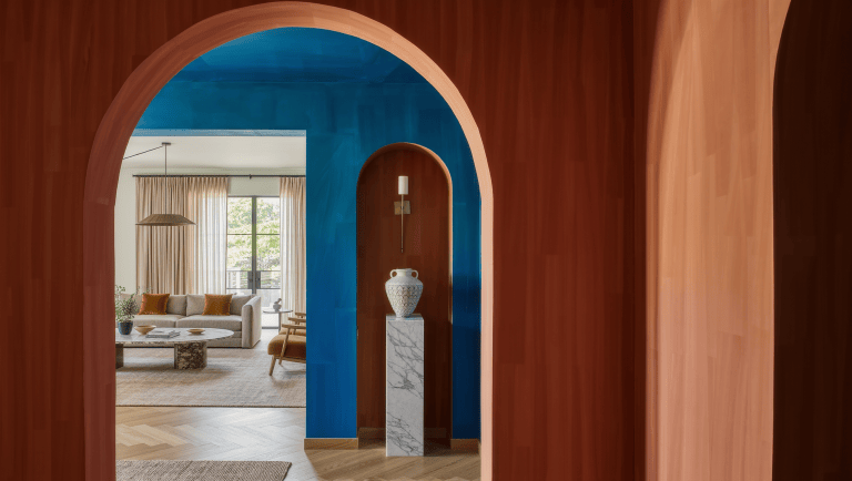 A wide, deep-set plaster archway with a terracotta reveal opens between a dining room and living room.