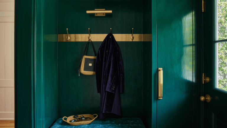 Open brass hooks holding a coat sit beside a closed lacquered cabinet in a jewel-toned entryway.