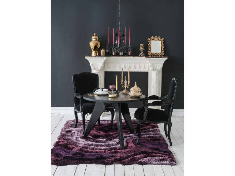 A white marble mantle holds gold candlesticks and objets against a black wall, with a round black lacquer table, black bergere chairs, and a plum shag rug in a dramatic formal room.