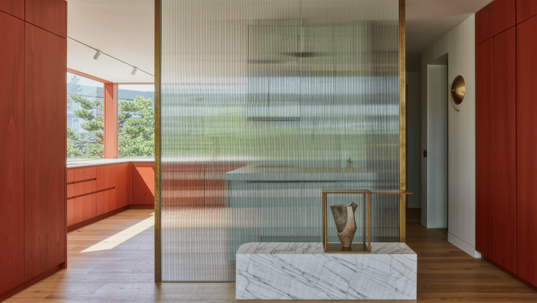 A fluted glass partition on a marble base divides a sunlit kitchen from the living room.