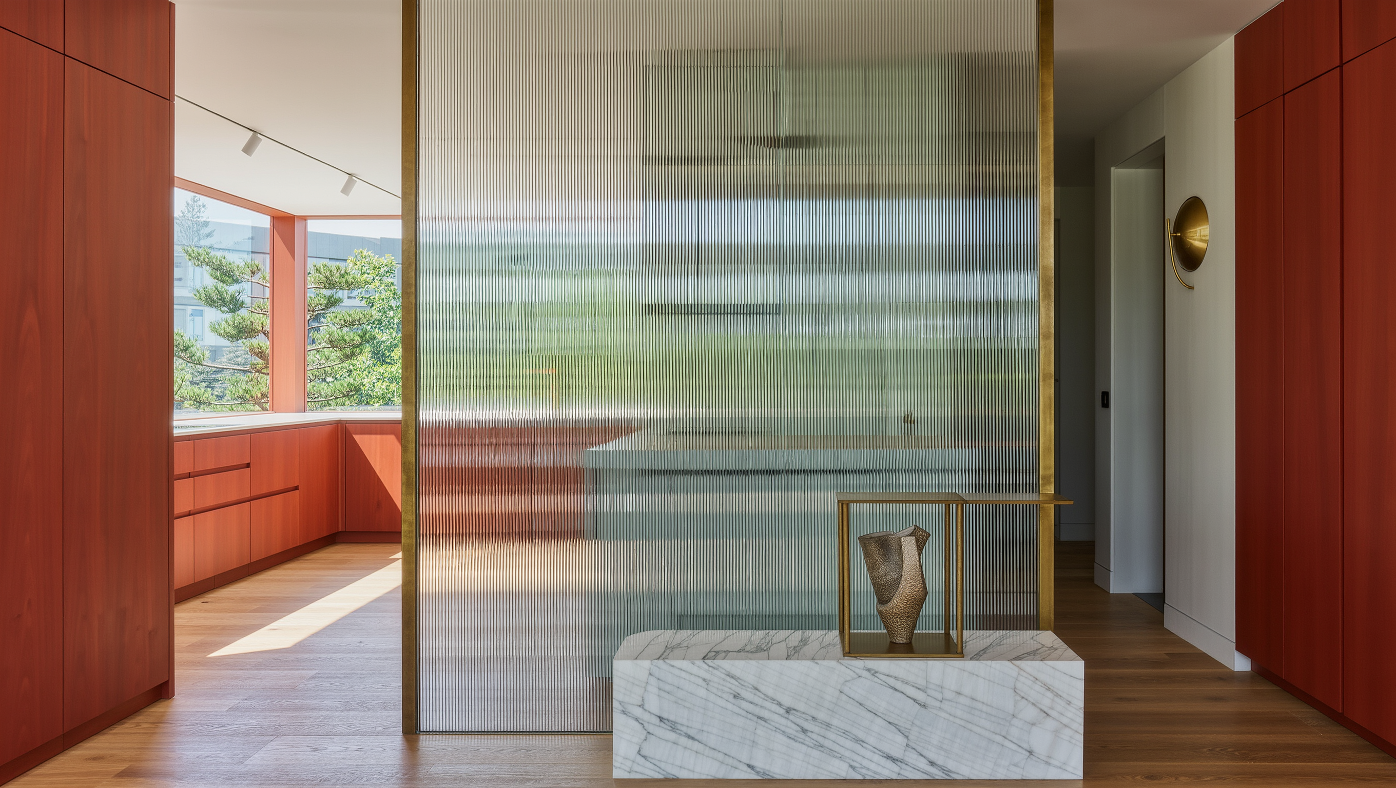 A fluted glass partition on a marble base divides a sunlit kitchen from the living room.