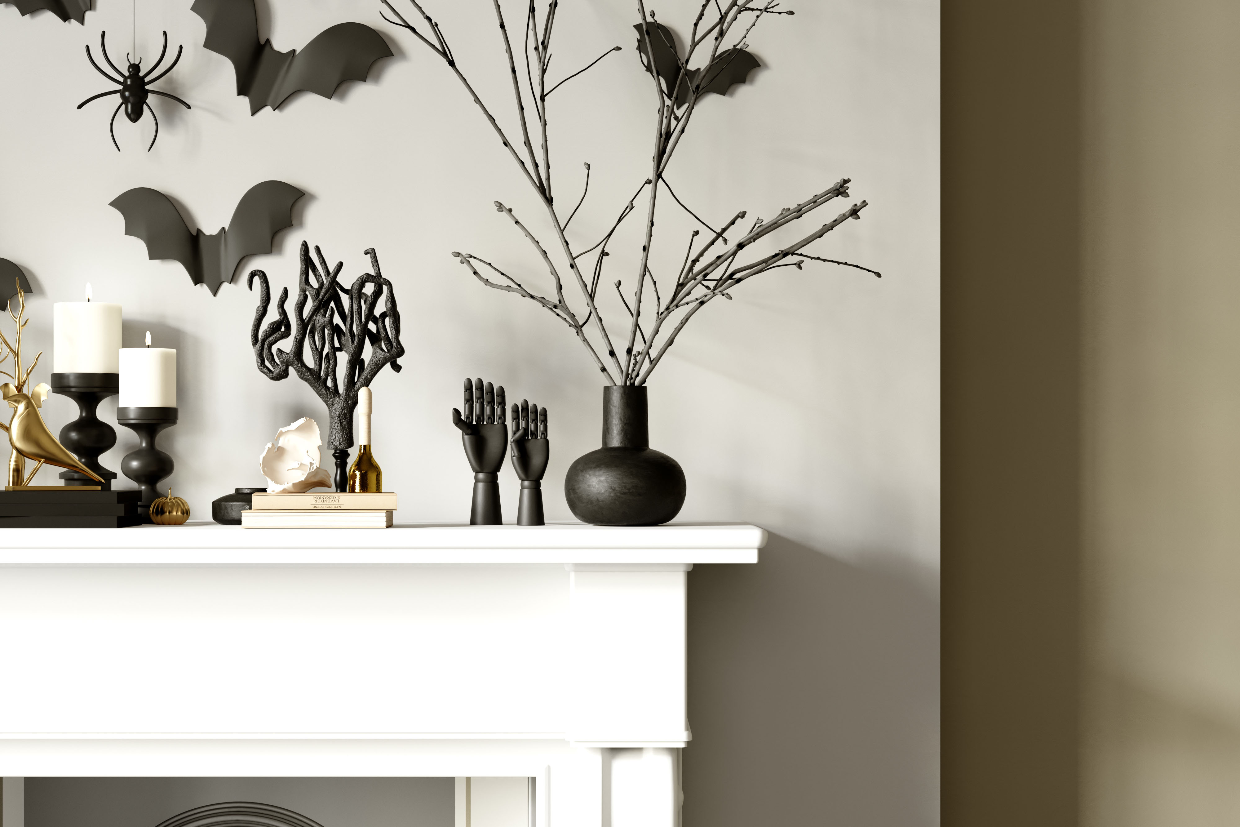 A white mantel is styled with black candlesticks, sculptural black branches, and paper bats and spiders trailing up the wall above it.