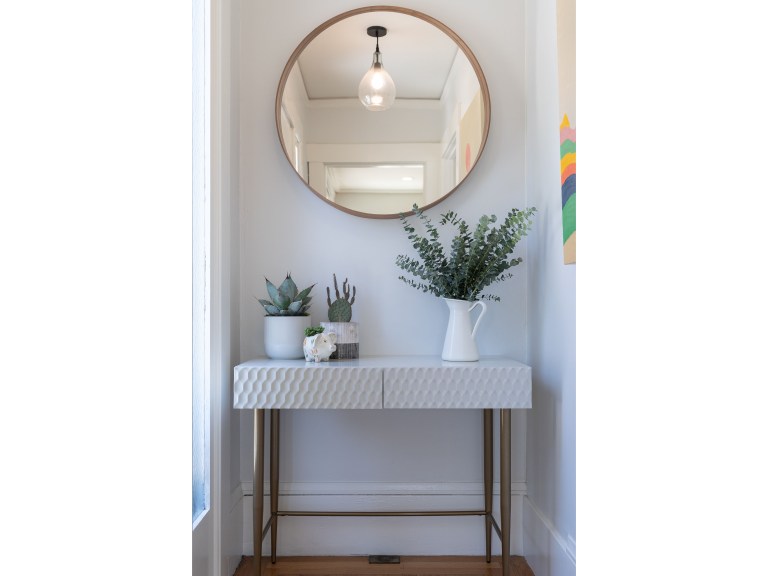 A slim marble-topped console with a round brass-framed mirror above hugs one wall of a hallway, leaving the floor path fully clear.
