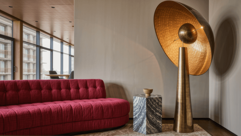 One oversized sculptural brass floor lamp dominates a living room corner beside a marble table.