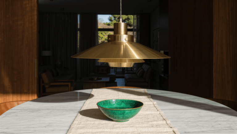 A brass pendant hangs low over a marble dining table, marking the zone from above.