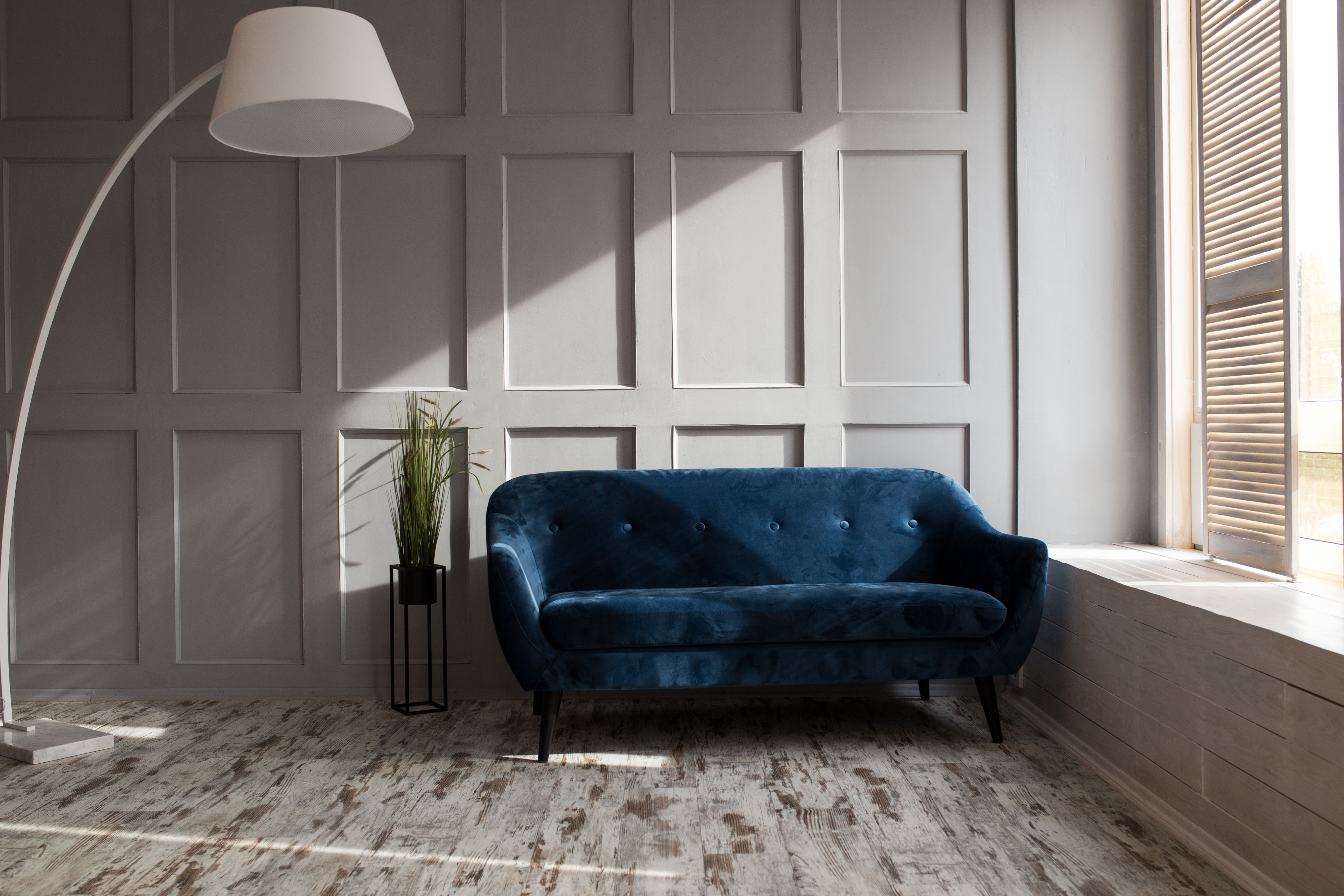 A sapphire velvet sofa sits against a deep-molded paneled wall in a sunlit loft corner, the paneling reading almost like a hidden door seam.